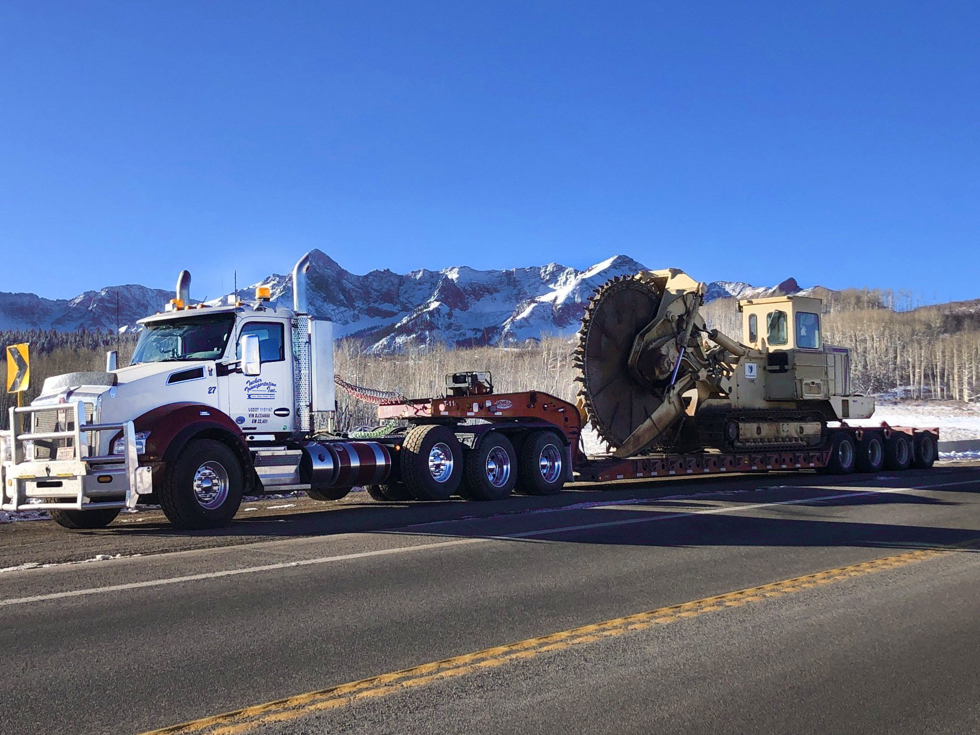 Heavy haul trucking trailer hauling oversized machinery near Telluride, Colorado with the San Juan Mountains in the background.